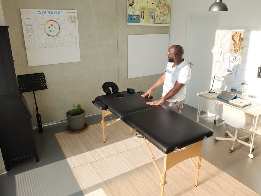 A physiotherapist standing next to a massage table in a modern, bright healthcare office.