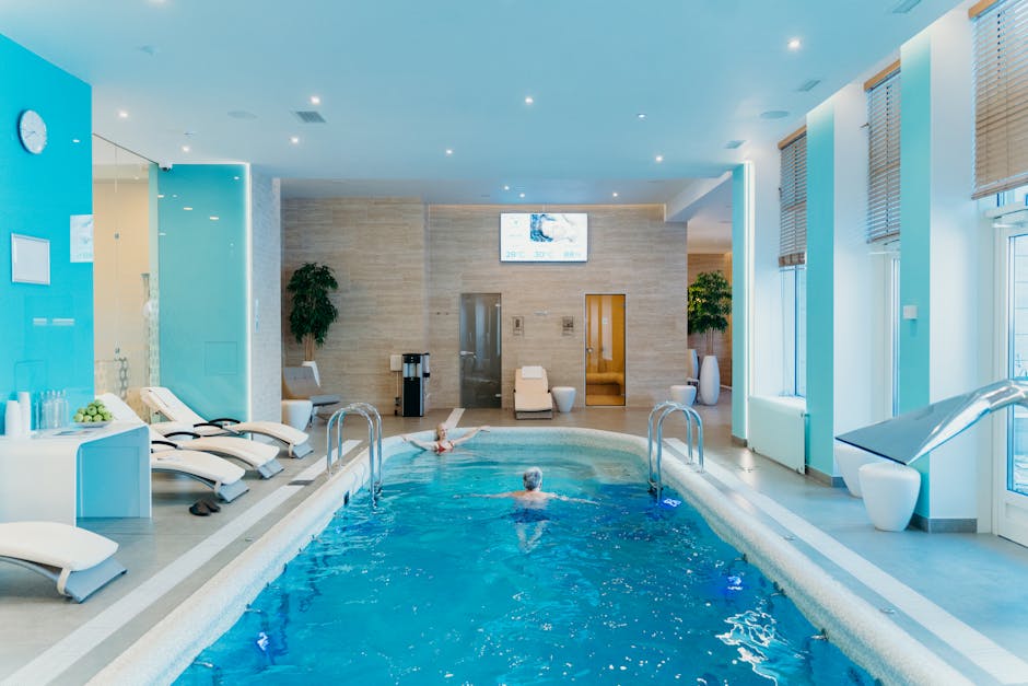 Luxurious indoor swimming pool in a modern spa with lounge chairs and soft lighting.